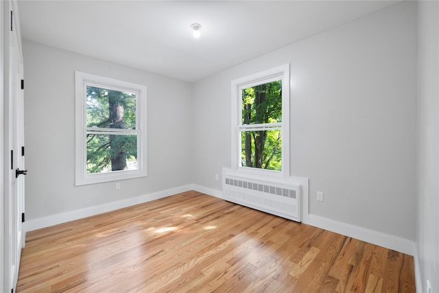 unfurnished room with a healthy amount of sunlight, light wood finished floors, radiator heating unit, and baseboards