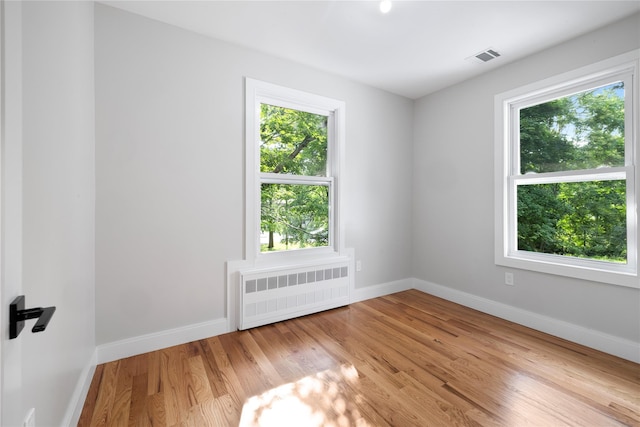 unfurnished room with radiator, baseboards, visible vents, and light wood finished floors