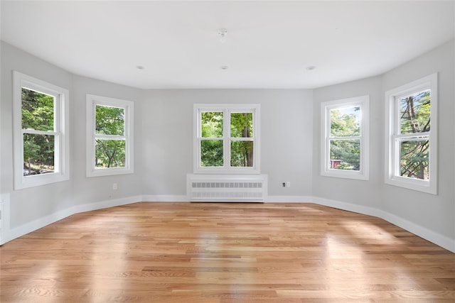 unfurnished room featuring a wealth of natural light, radiator, light wood-style flooring, and baseboards