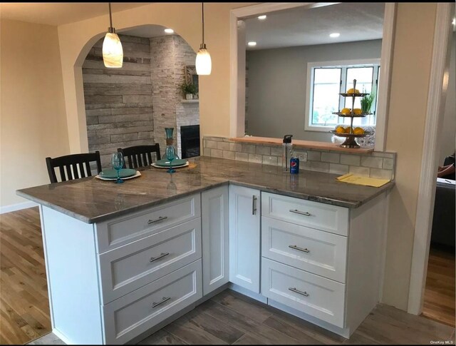 bar with dark wood-style floors, arched walkways, recessed lighting, decorative backsplash, and hanging light fixtures