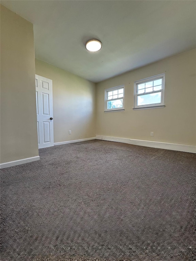 unfurnished room featuring dark carpet and baseboards