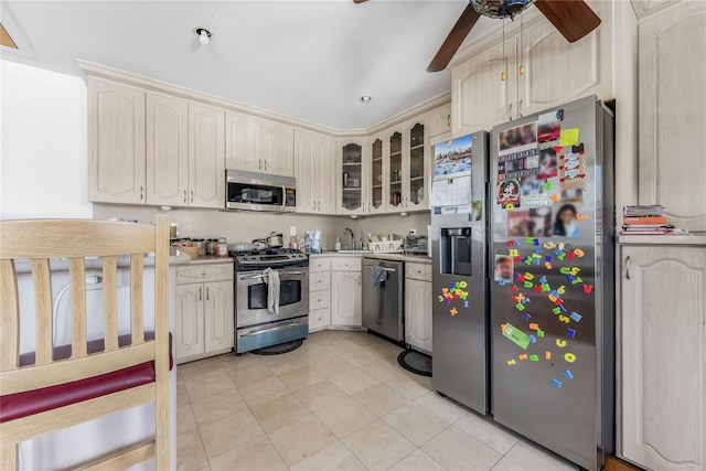 kitchen featuring stainless steel appliances, light countertops, glass insert cabinets, a ceiling fan, and a sink