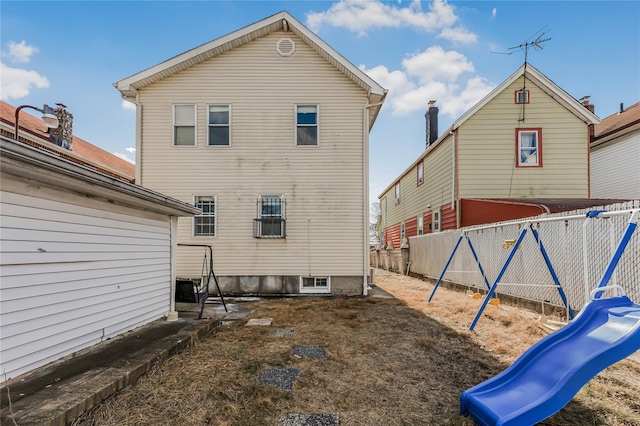 back of property featuring a playground and fence