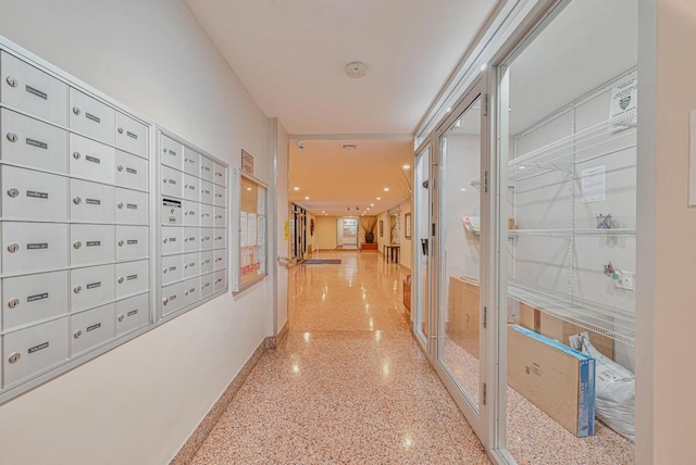 hallway featuring light speckled floor, mail area, and baseboards