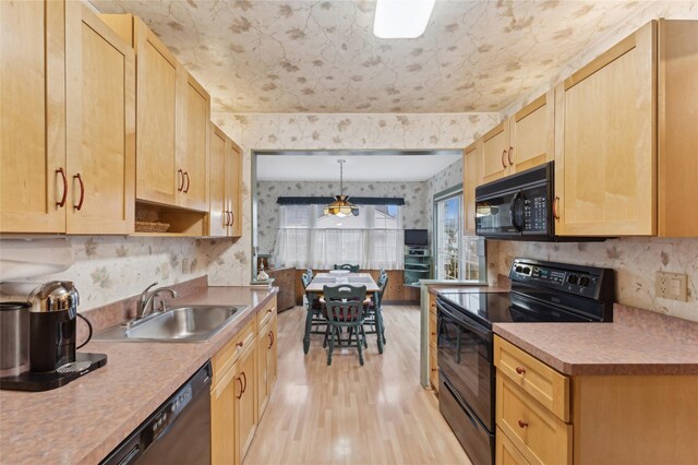 kitchen featuring wallpapered walls, decorative light fixtures, light countertops, black appliances, and a sink