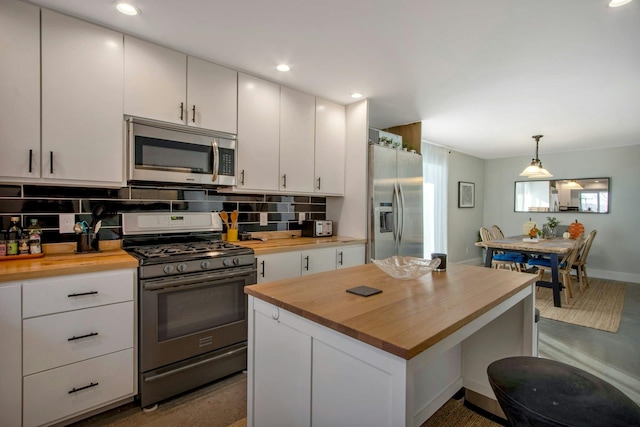 kitchen featuring butcher block countertops, tasteful backsplash, stainless steel appliances, white cabinets, and hanging light fixtures