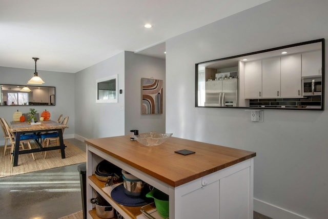 kitchen featuring baseboards, open shelves, stainless steel appliances, decorative light fixtures, and butcher block counters