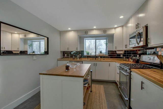 kitchen featuring wooden counters, baseboards, decorative backsplash, stainless steel appliances, and a sink