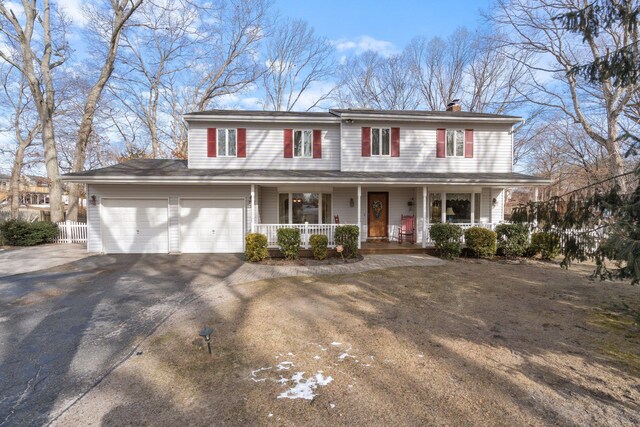 view of front of home with covered porch, driveway, a chimney, and fence