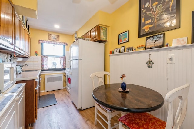 kitchen with white appliances, light wood-style floors, light countertops, brown cabinets, and radiator heating unit