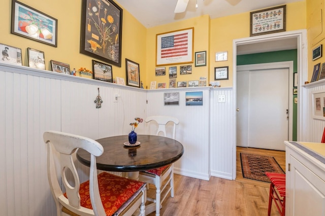 dining area with light wood-style floors, a wainscoted wall, and ceiling fan