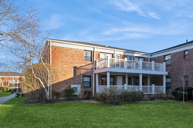 back of property with a balcony, a lawn, and brick siding