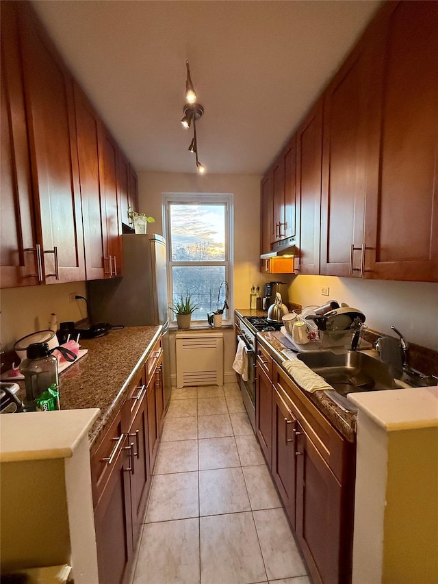 kitchen featuring light tile patterned flooring, high end stove, under cabinet range hood, a sink, and rail lighting