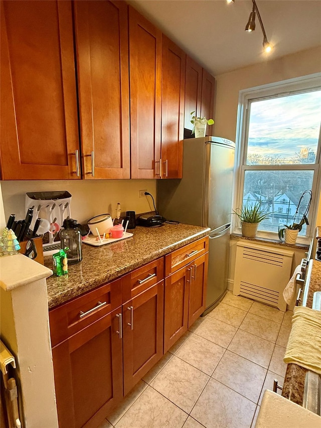 kitchen with brown cabinets, freestanding refrigerator, dark stone counters, and light tile patterned flooring