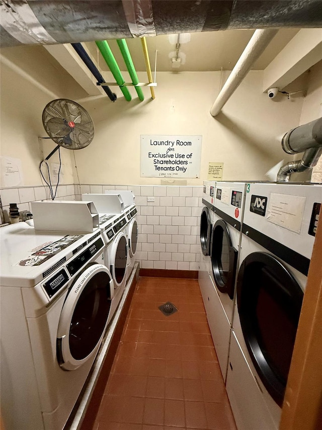 common laundry area with dark tile patterned flooring, a wainscoted wall, washer and clothes dryer, and tile walls