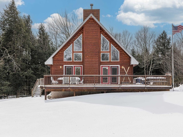 snow covered back of property featuring a chimney, log veneer siding, and a deck