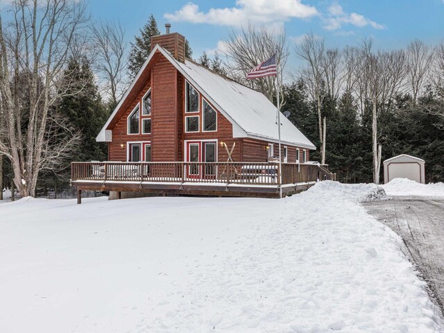 snow covered back of property featuring a deck, a chimney, and a detached garage