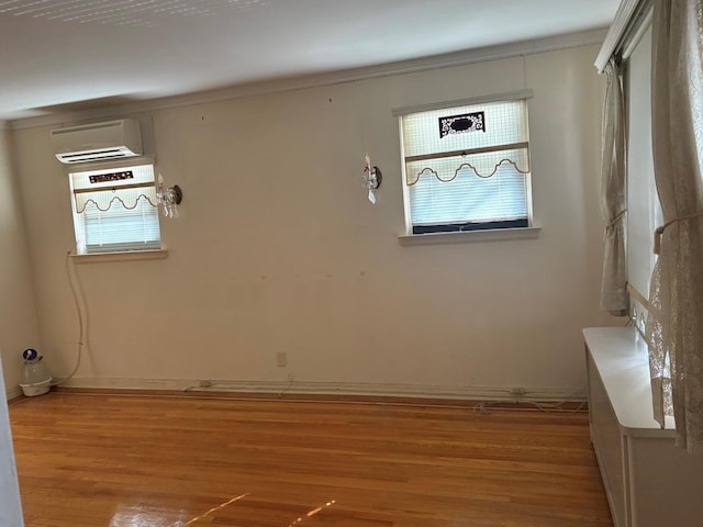 empty room featuring baseboards, a wall unit AC, light wood-style flooring, and a healthy amount of sunlight