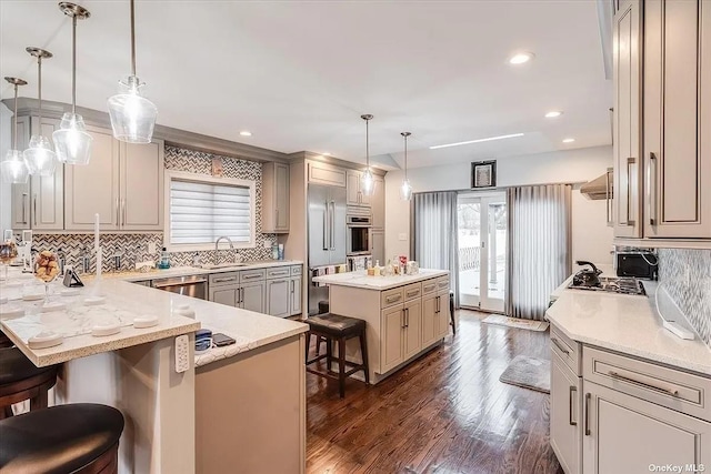 kitchen featuring a center island, decorative light fixtures, stainless steel appliances, a peninsula, and a kitchen bar