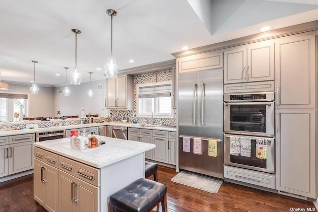 kitchen with pendant lighting, appliances with stainless steel finishes, a kitchen island, light stone countertops, and a kitchen breakfast bar