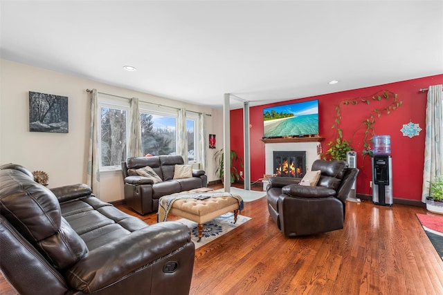 living area with a glass covered fireplace, baseboards, recessed lighting, and wood finished floors