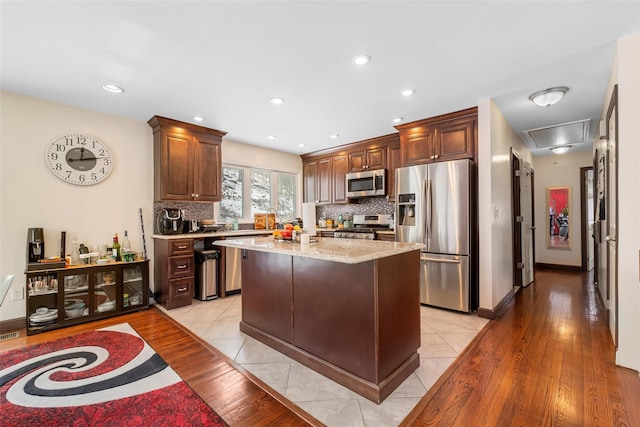 kitchen with light stone counters, light wood finished floors, stainless steel appliances, backsplash, and a kitchen island