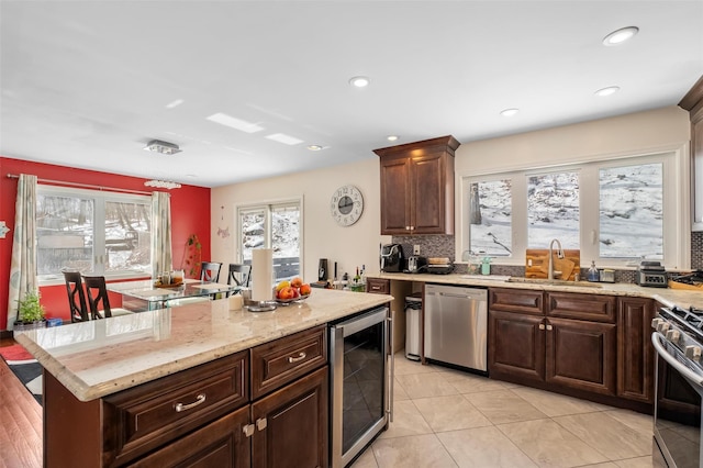 kitchen with wine cooler, a sink, appliances with stainless steel finishes, backsplash, and light stone countertops