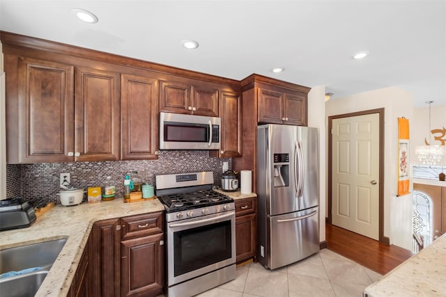 kitchen featuring appliances with stainless steel finishes, a sink, light stone counters, and tasteful backsplash