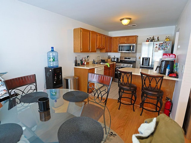 kitchen featuring light countertops, visible vents, appliances with stainless steel finishes, brown cabinetry, and light wood-type flooring