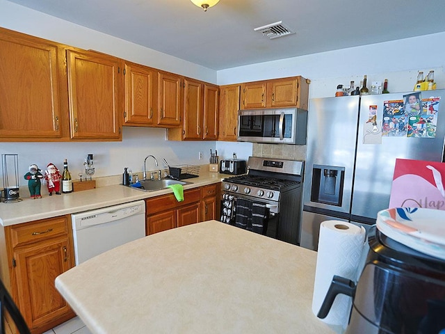 kitchen with brown cabinets, stainless steel appliances, light countertops, visible vents, and a sink