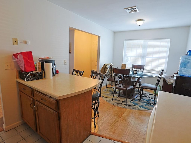 kitchen with brown cabinets, light countertops, visible vents, light wood-type flooring, and a kitchen breakfast bar