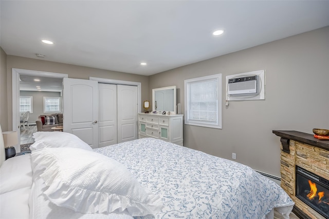 bedroom with recessed lighting, a closet, a baseboard radiator, an AC wall unit, and a stone fireplace