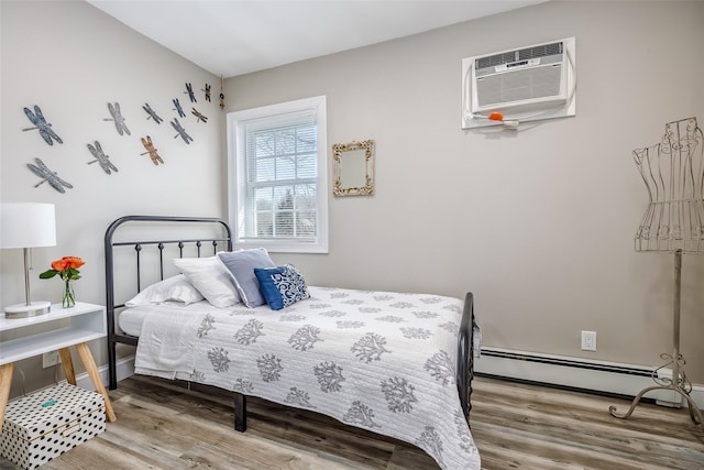 bedroom with baseboard heating, a wall mounted air conditioner, wood finished floors, and baseboards