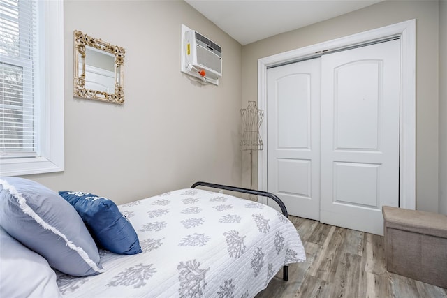 bedroom with multiple windows, a wall mounted AC, a closet, and light wood-style floors