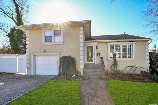 tri-level home with decorative driveway, fence, and stucco siding