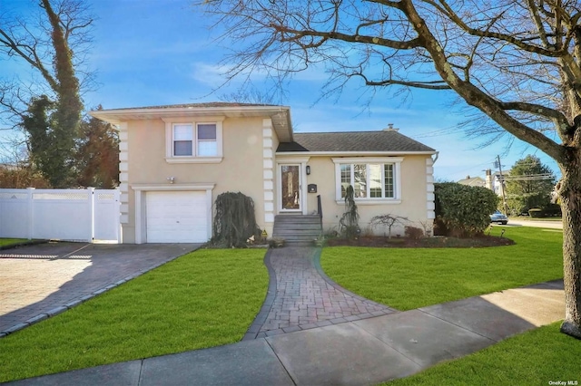 tri-level home featuring driveway, a front lawn, fence, and stucco siding