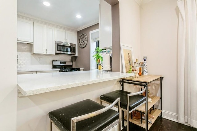 kitchen with light stone counters, backsplash, appliances with stainless steel finishes, white cabinetry, and a peninsula