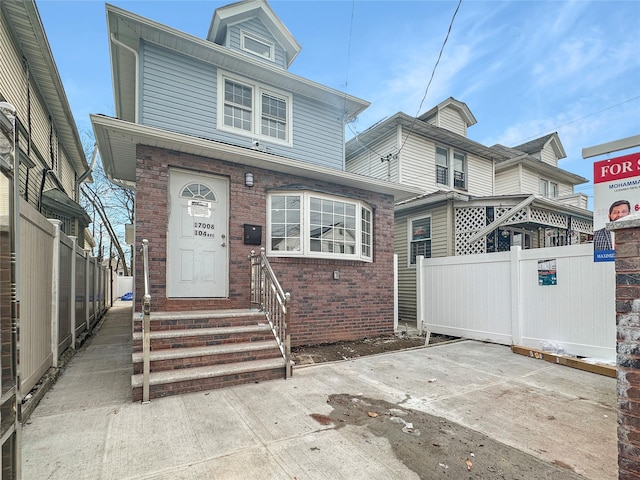 american foursquare style home featuring entry steps, brick siding, and fence