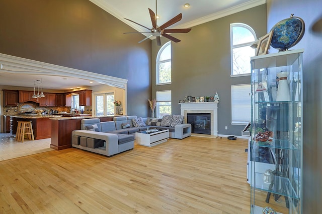 living room featuring light wood-style flooring, ornamental molding, ceiling fan, and a glass covered fireplace