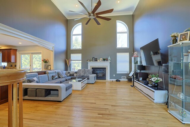 living area with ornamental molding, plenty of natural light, a glass covered fireplace, and light wood-style flooring