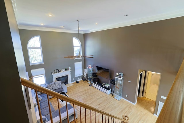 living area featuring wood finished floors, a ceiling fan, stairs, a glass covered fireplace, and crown molding