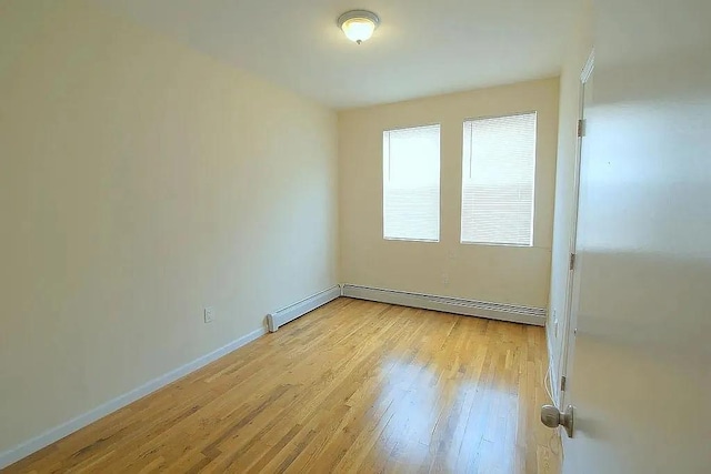 spare room with light wood-style flooring, a baseboard heating unit, and baseboards