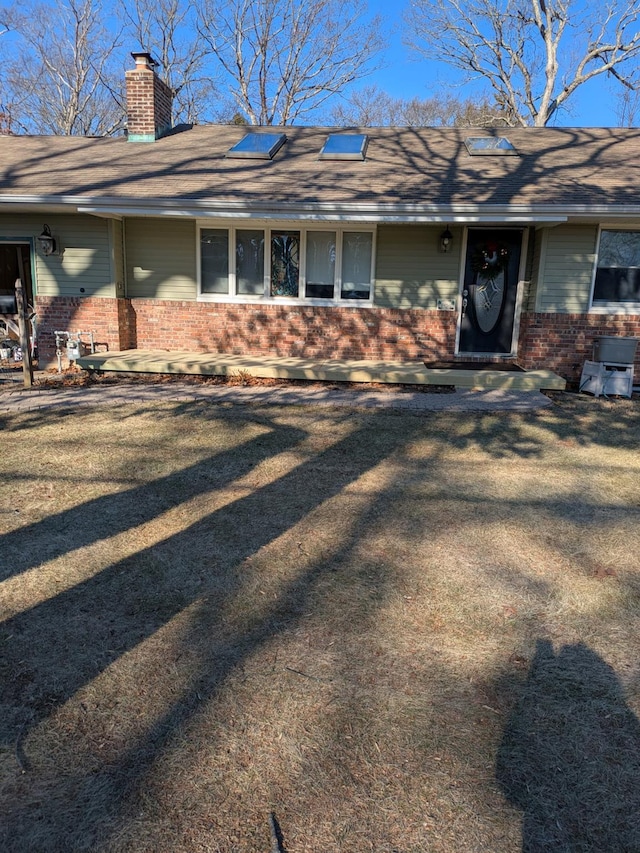 view of front of home with roof with shingles, brick siding, a chimney, and a front yard