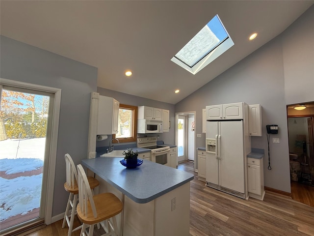 kitchen with a peninsula, white appliances, a skylight, white cabinetry, and dark wood-style floors