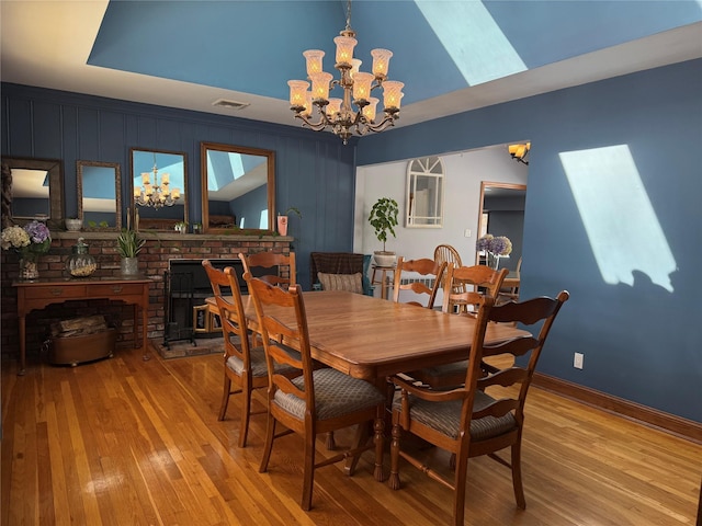 dining room featuring light wood-style flooring, a fireplace, visible vents, and a notable chandelier