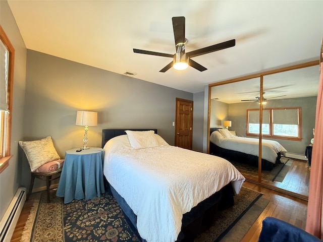 bedroom featuring visible vents, a baseboard heating unit, a ceiling fan, wood finished floors, and baseboards