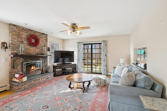 living area featuring ceiling fan, a fireplace, wood finished floors, and a baseboard radiator