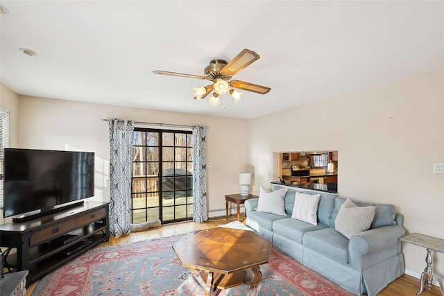 living room featuring a baseboard heating unit, a ceiling fan, baseboards, and wood finished floors