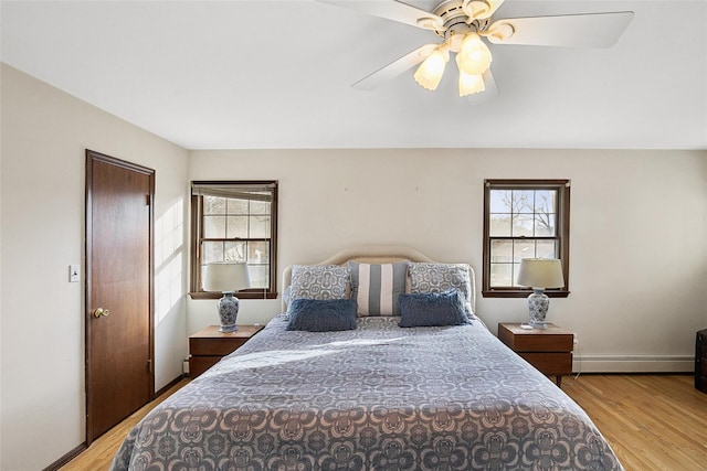 bedroom with light wood finished floors, multiple windows, and baseboard heating