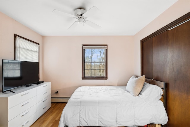 bedroom with light wood-type flooring, ceiling fan, and a baseboard heating unit